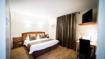 Habitación de hotel con una cama de madera, un escritorio con una silla, un televisor sobre el escritorio y una ventana con cortinas.