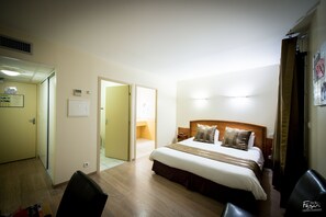 A hotel room with a bed, a chair, a desk, and a door leading to another room. - Hotel Le Lion D'or (Saint-Geniez-d'Olt-et-d'Aubrac)