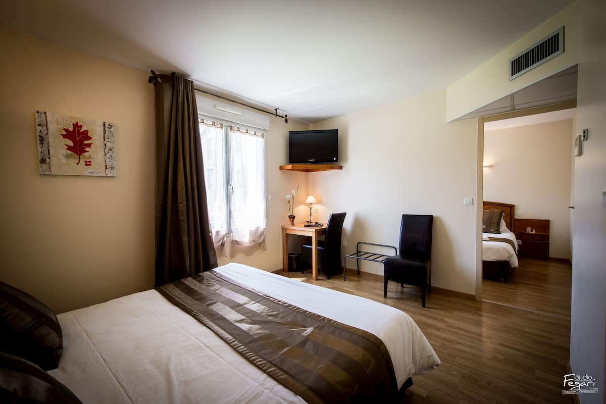 Une chambre d’hôtel avec un lit, un bureau, une chaise, une télévision et une fenêtre avec des rideaux.