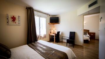 A hotel room with a bed, a desk, a chair, a TV, and a window with curtains.