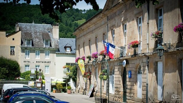 A hotel with a stone facade, multiple windows, and balconies with flowers. - Hotel Le Lion D'or (Saint-Geniez-d'Olt-et-d'Aubrac)