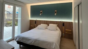 A modern bedroom with a large bed, a sliding glass door to the outside, and a teal accent wall. - Hotel Le Lion D'or (Saint-Geniez-d'Olt-et-d'Aubrac)