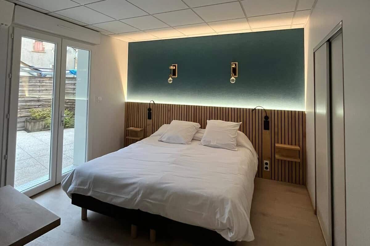 Une chambre à coucher moderne avec un grand lit, une porte-fenêtre coulissante donnant sur l’extérieur et un mur d’accent de couleur turquoise.