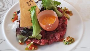 A white plate with a unique design, containing a dish with a poached egg, greens, and a piece of bread. - Hotel Le Lion D'or (Saint-Geniez-d'Olt-et-d'Aubrac)