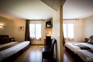 A hotel room with two beds, a TV mounted on the wall, a desk with a lamp, and a chair. - Hotel Le Lion D'or (Saint-Geniez-d'Olt-et-d'Aubrac)