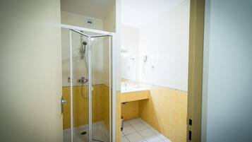 Un baño con ducha de vidrio, lavamanos y paredes de azulejos amarillos.