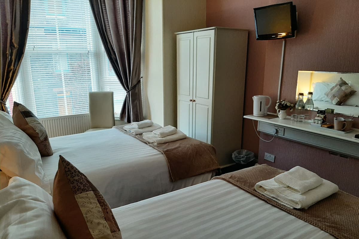 A hotel room with two beds, a wardrobe, a television, and a small table with toiletries.