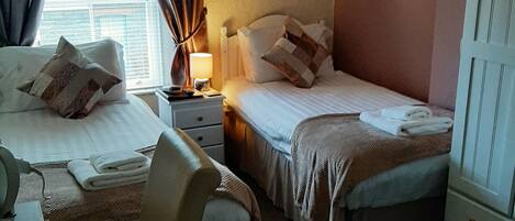 Habitación de hotel con dos camas, un escritorio y una silla. Cuenta con una ventana con cortinas, una lámpara en la mesita de noche y un cuadro en la pared.