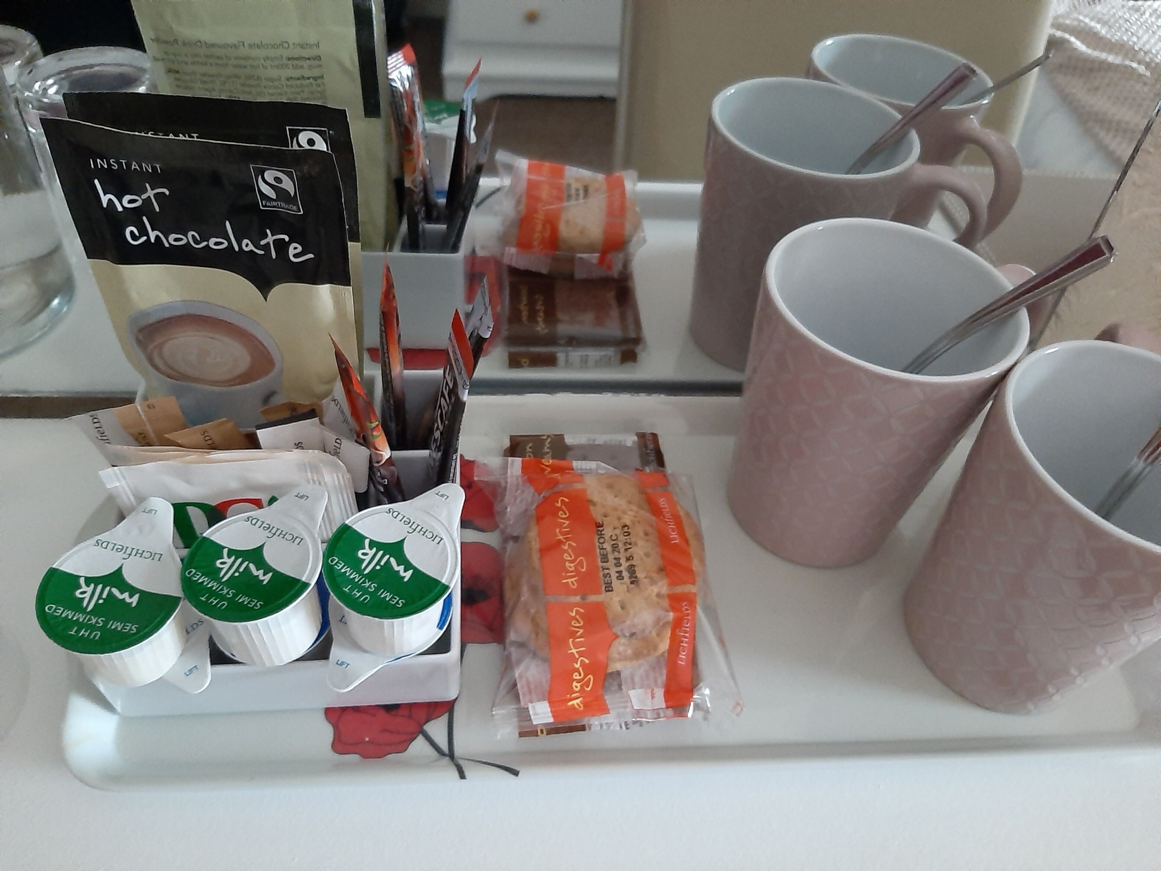 A table with instant hot chocolate packets, milk packets, and cookies.