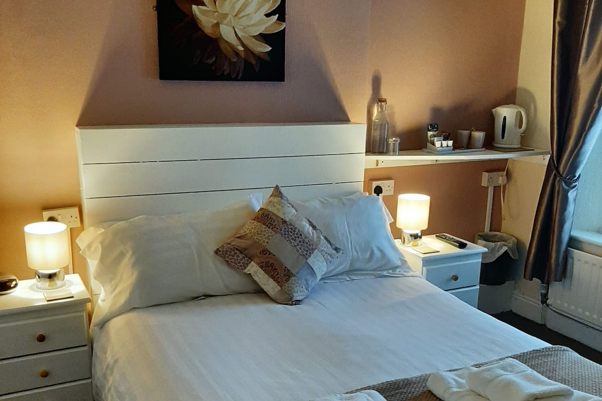 A neatly made bed with white linens, a decorative pillow, and folded towels on a woven mat.