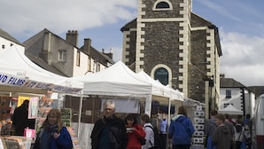 A historic building with a clock tower, surrounded by market stalls and people. - Lyndhurst Guest House (Keswick)