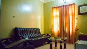 A living room with a sofa, a glass coffee table, and a television mounted on the wall. - Golden Destiny Hotel Limited (Lagos)