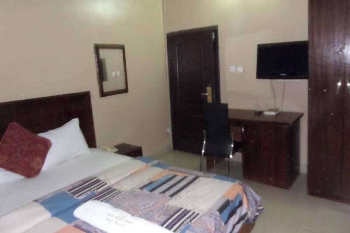A hotel room with a bed, a desk, a chair, a television, and a wardrobe.