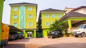 A multi-story building with a green facade, multiple windows, and a parking area with several cars. - Golden Destiny Hotel Limited (Lagos)