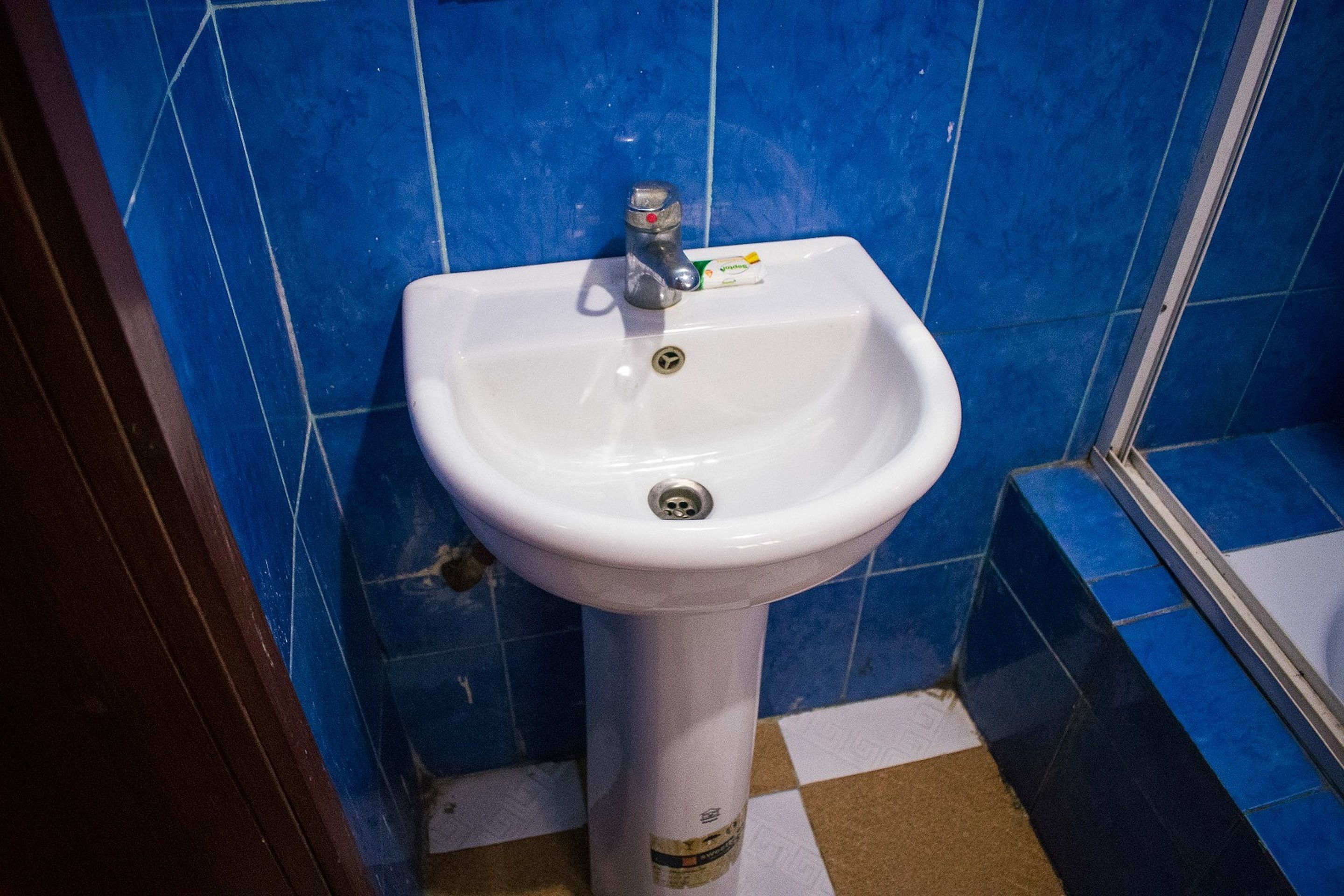 A white pedestal sink with a faucet and soap dispenser in a bathroom with blue tiled walls.