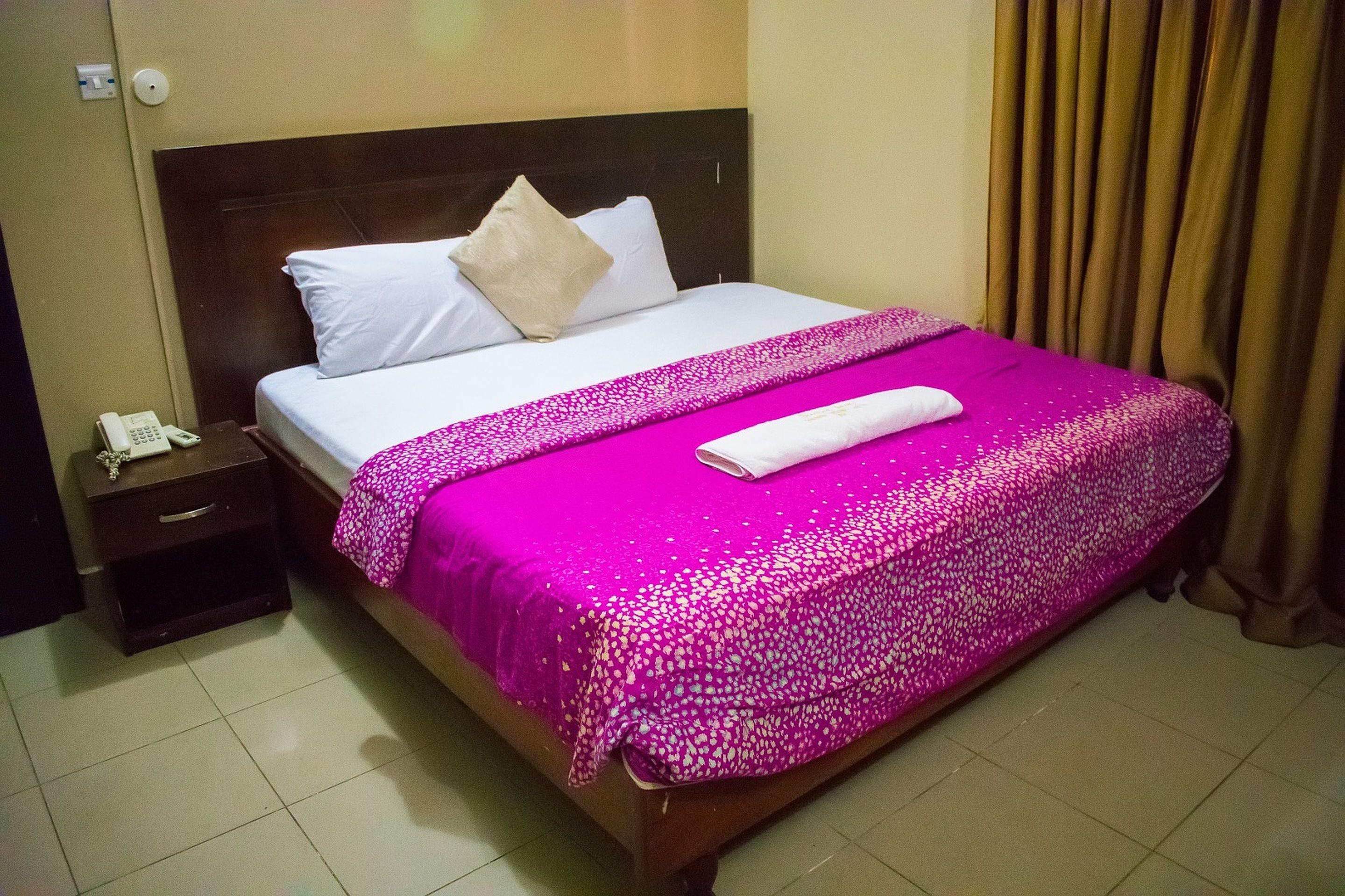 A hotel room with a bed, a nightstand, a telephone, and a curtain.
