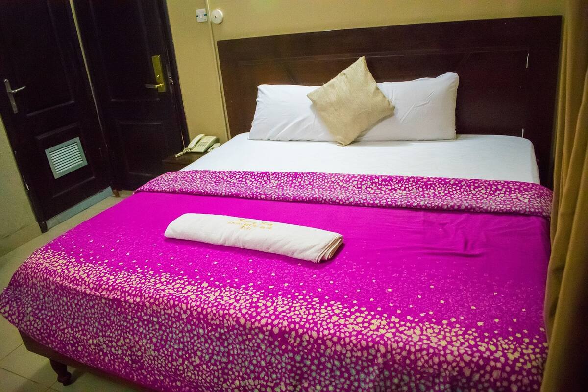 A hotel room with a bed, a bedside telephone, and a door with a handle.