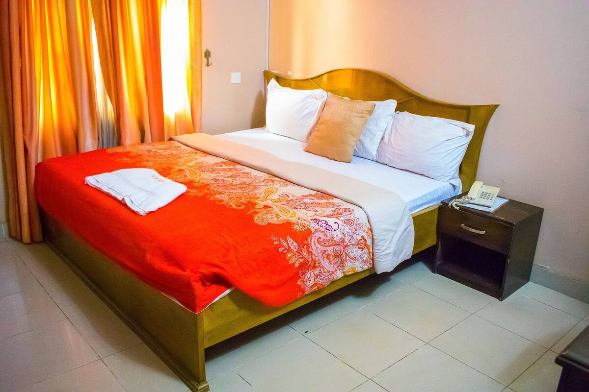 A neatly made bed with a red and white bedspread, a wooden headboard, and a nightstand with a telephone.