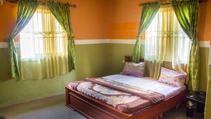 Une chambre à coucher avec un lit en bois, des rideaux verts et un sol carrelé.