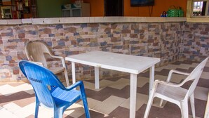 Un espace patio avec une table blanche et quatre chaises en plastique, dont une bleue et trois blanches.