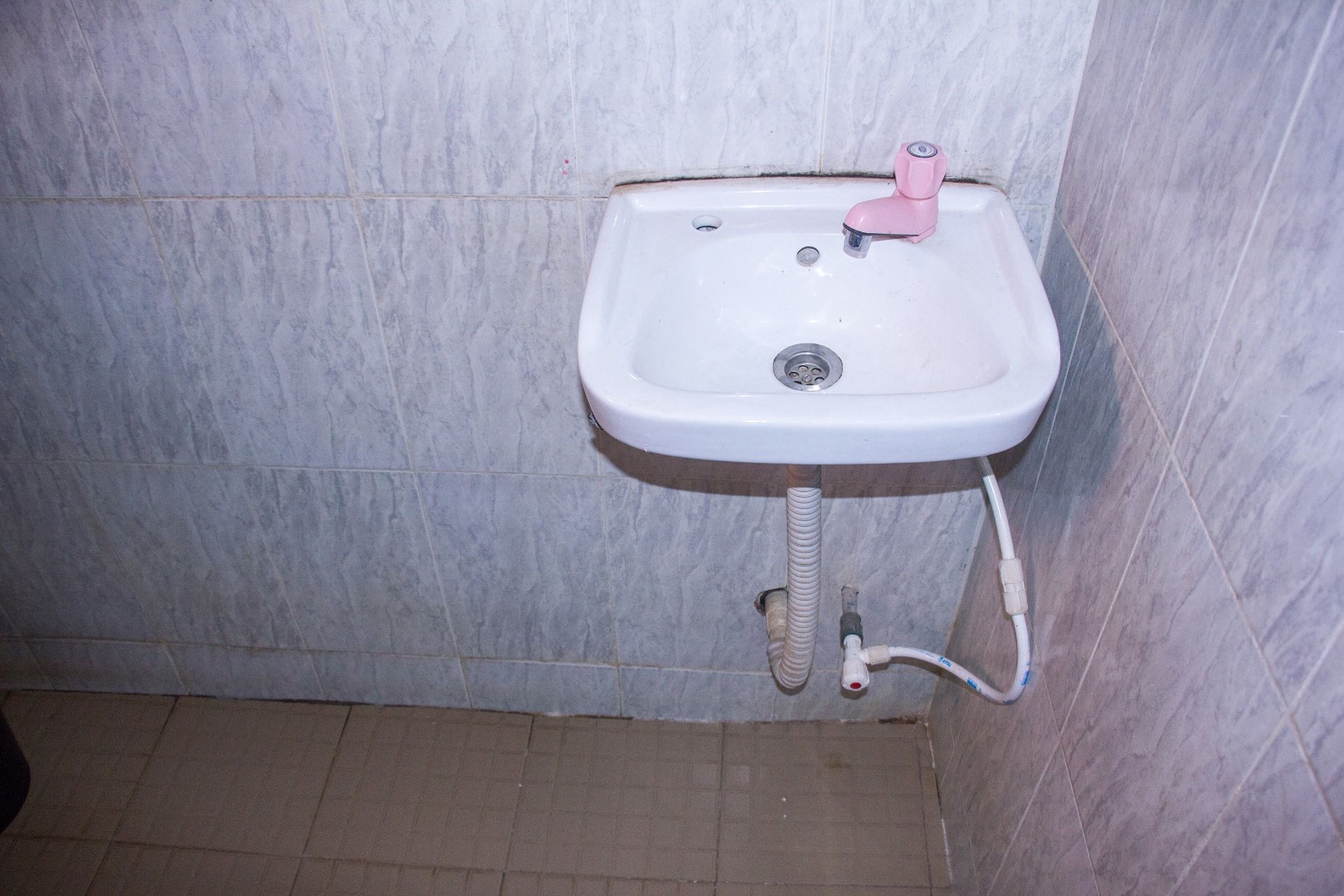 Une salle de bain avec un lavabo blanc, un robinet rose et un drain apparent.