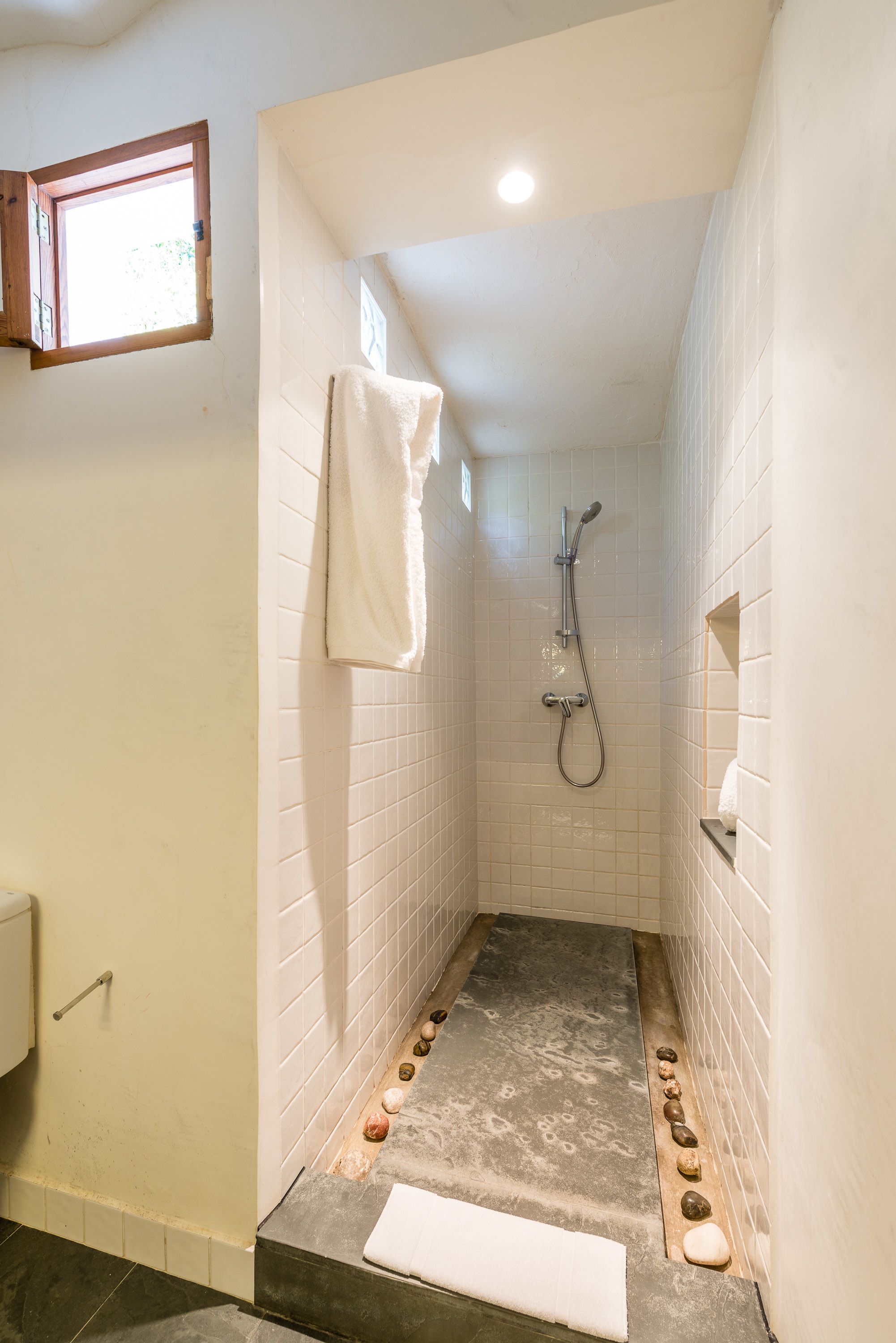Ein kleiner Duschbereich mit Fliesen, einer Handbrause, einem Handtuch an der Wand und einem Ablagefach für Pflegeprodukte.