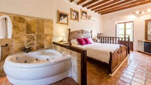 Un dormitorio con una bañera grande, vigas de madera en el techo y una cama con cabecero de madera.