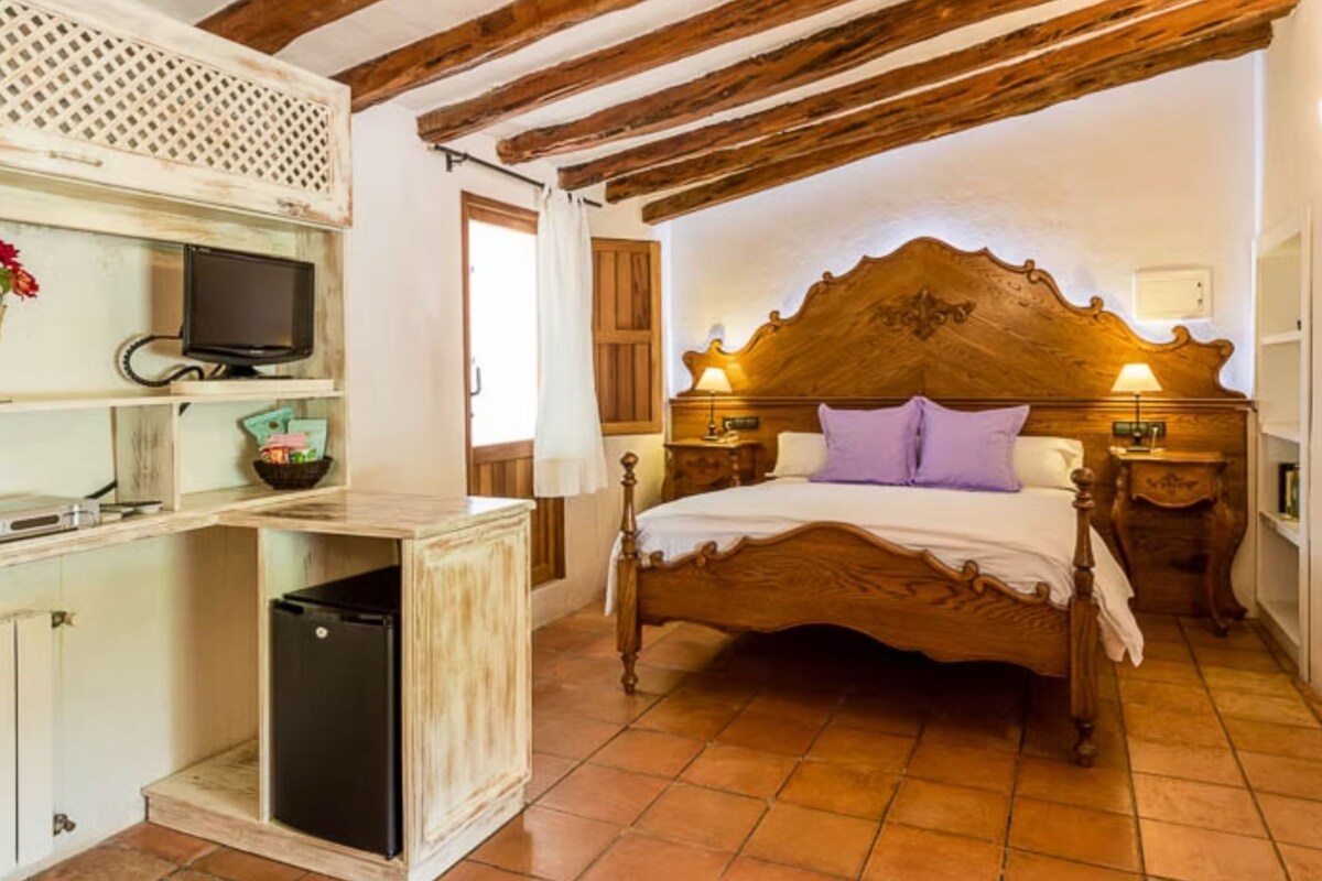 Un dormitorio con una cama de madera, un televisor en un estante y un refrigerador pequeño.