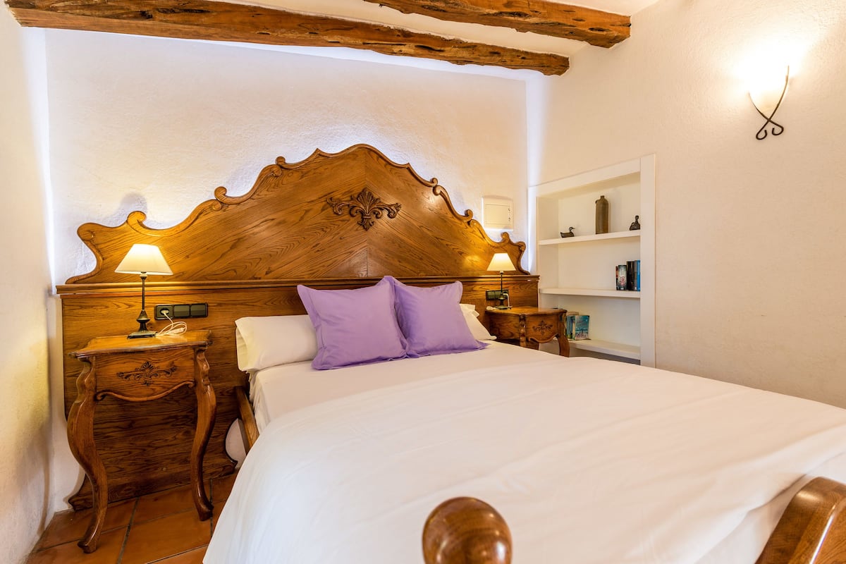 A neatly made bed with a wooden headboard, two bedside lamps, and a shelf with toiletries.