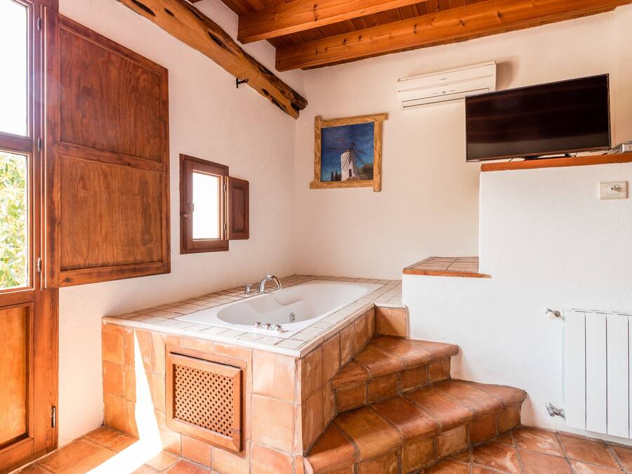 A bathroom with a bathtub, wooden steps, a window, and a painting on the wall.