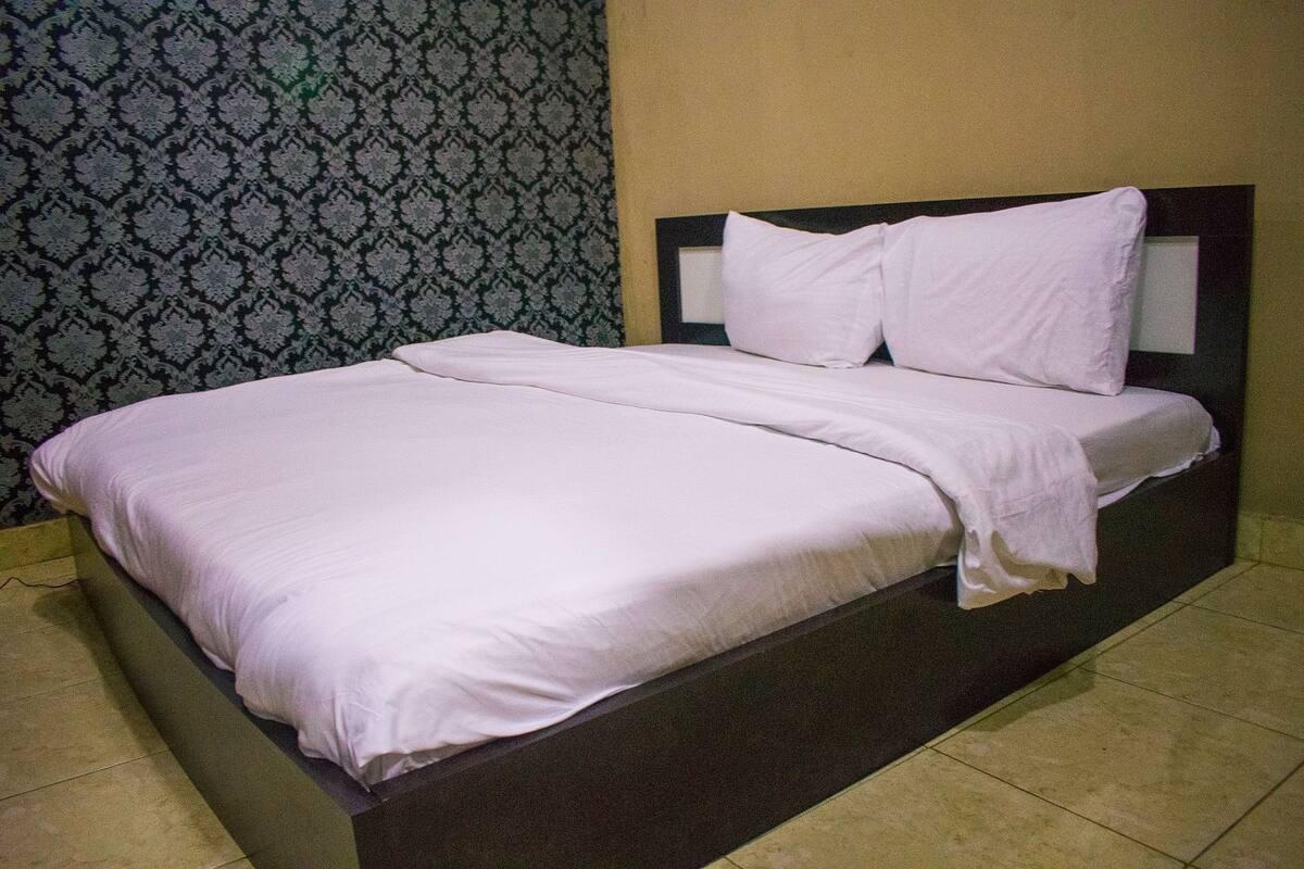 A bed with white bedding in a room with patterned wallpaper and a plain wall.