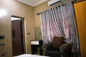 Une chambre d’hôtel avec un lit, un bureau, une chaise, un oreiller marron et un rideau à motifs floraux.