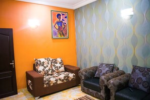 Un salon avec deux canapés, dont l’un est agrémenté de coussins à motifs floraux et l’autre de coussins à motifs variés, un tableau au mur et un papier peint à motifs.