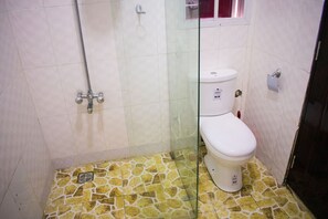 Une salle de bain avec douche, toilettes et carrelage au sol.