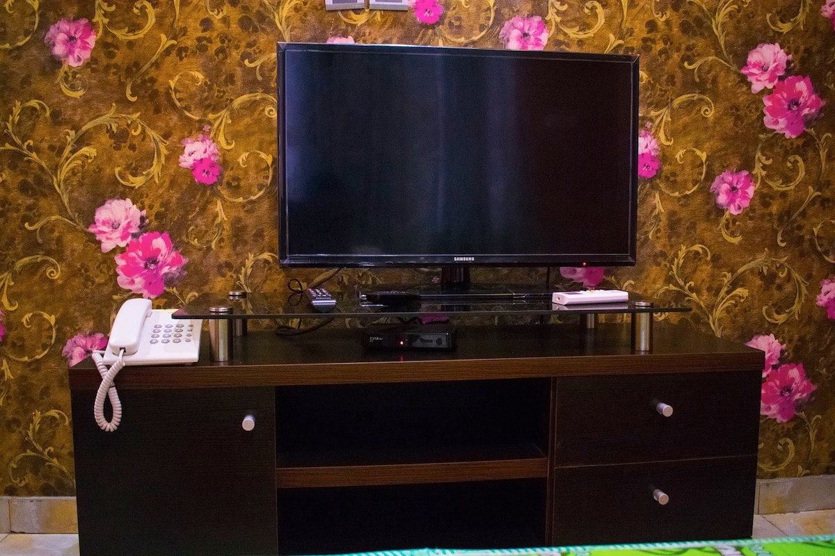 A flat-screen TV on a wooden entertainment unit with a telephone and remote control.