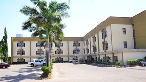 A multi-story building with a flat roof, air conditioning units, and a parking area with cars. - De' Nevilla Hotel (Kaduna)