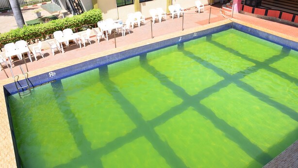 A swimming pool with a tiled edge, surrounded by white lounge chairs and a tiled deck area. - De' Nevilla Hotel (Kaduna)