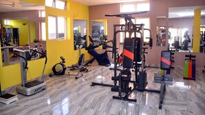 A gym with exercise equipment, mirrors, and a yellow wall. - De' Nevilla Hotel (Kaduna)