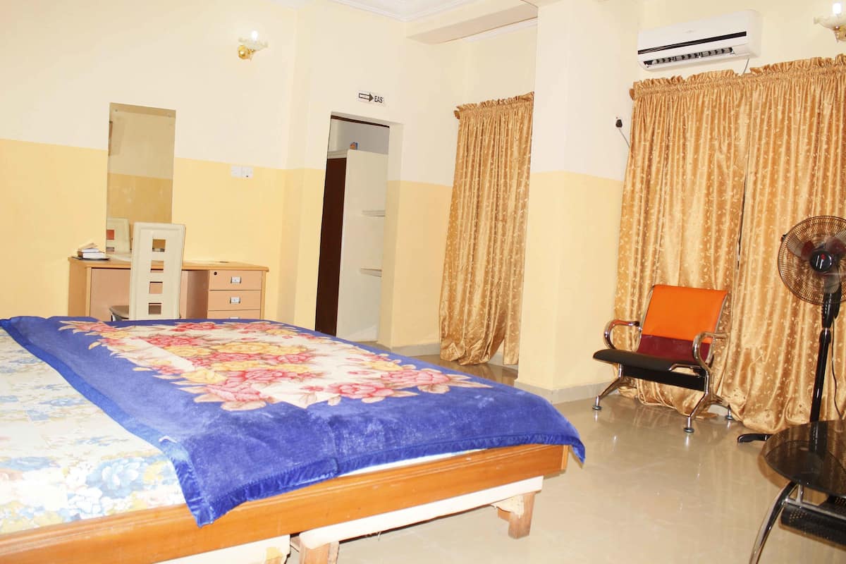 A bedroom with a bed, a desk, a chair, an air conditioner, and curtains.