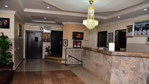 Zona de recepción de un hotel con mostrador de mármol, candelabro, cuadros enmarcados y un reloj en la pared.