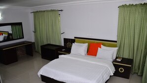 Un dormitorio ordenado con una cama grande, una mesita de noche, un aparador y un espejo.