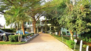 Un sendero pavimentado bordeado de árboles y arbustos, que conduce a un edificio de varios pisos.