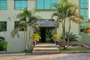A building with a concrete entrance, potted palm trees, and a paved walkway leading to the entrance. - Green Suites Villa (Kaduna)