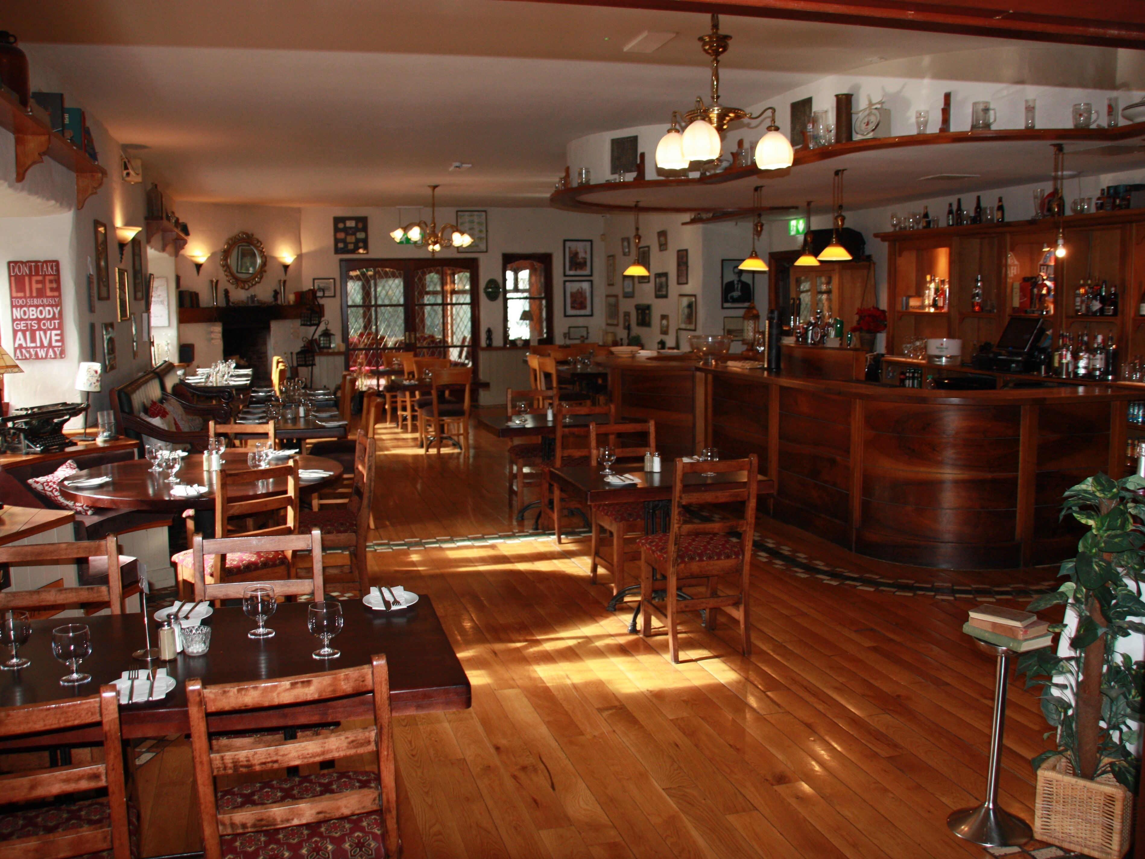 A restaurant with wooden tables and chairs, a bar area, and various hanging lights.