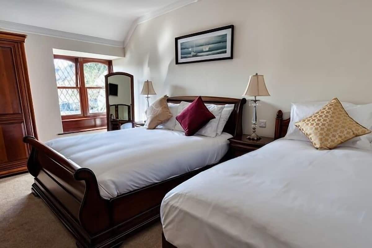 A hotel room with two beds, a window, a framed picture on the wall, and a mirror.
