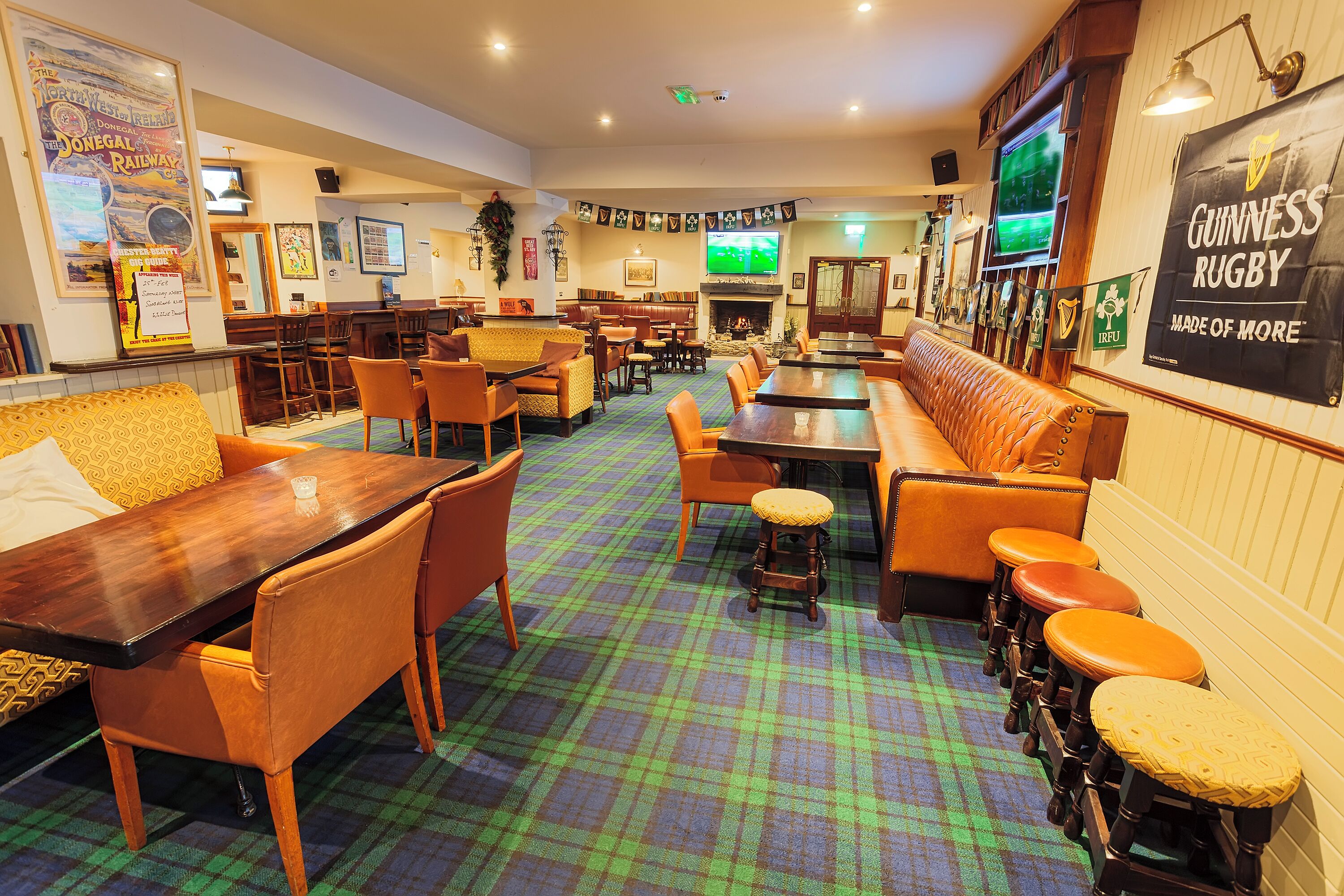 A pub with wooden furniture, a green plaid carpet, and a television screen displaying a sports event.