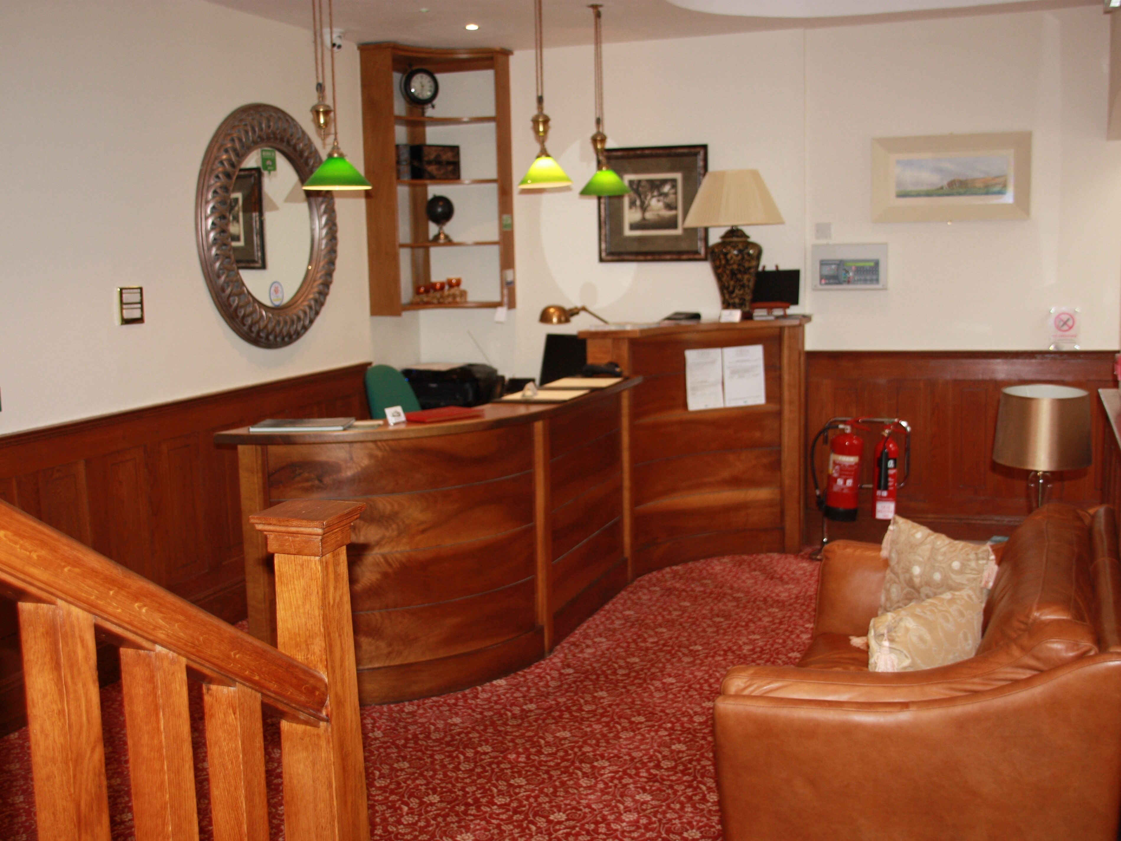 Un hall con mostrador de recepción, una escalera de madera, un sofá de cuero y un extintor.