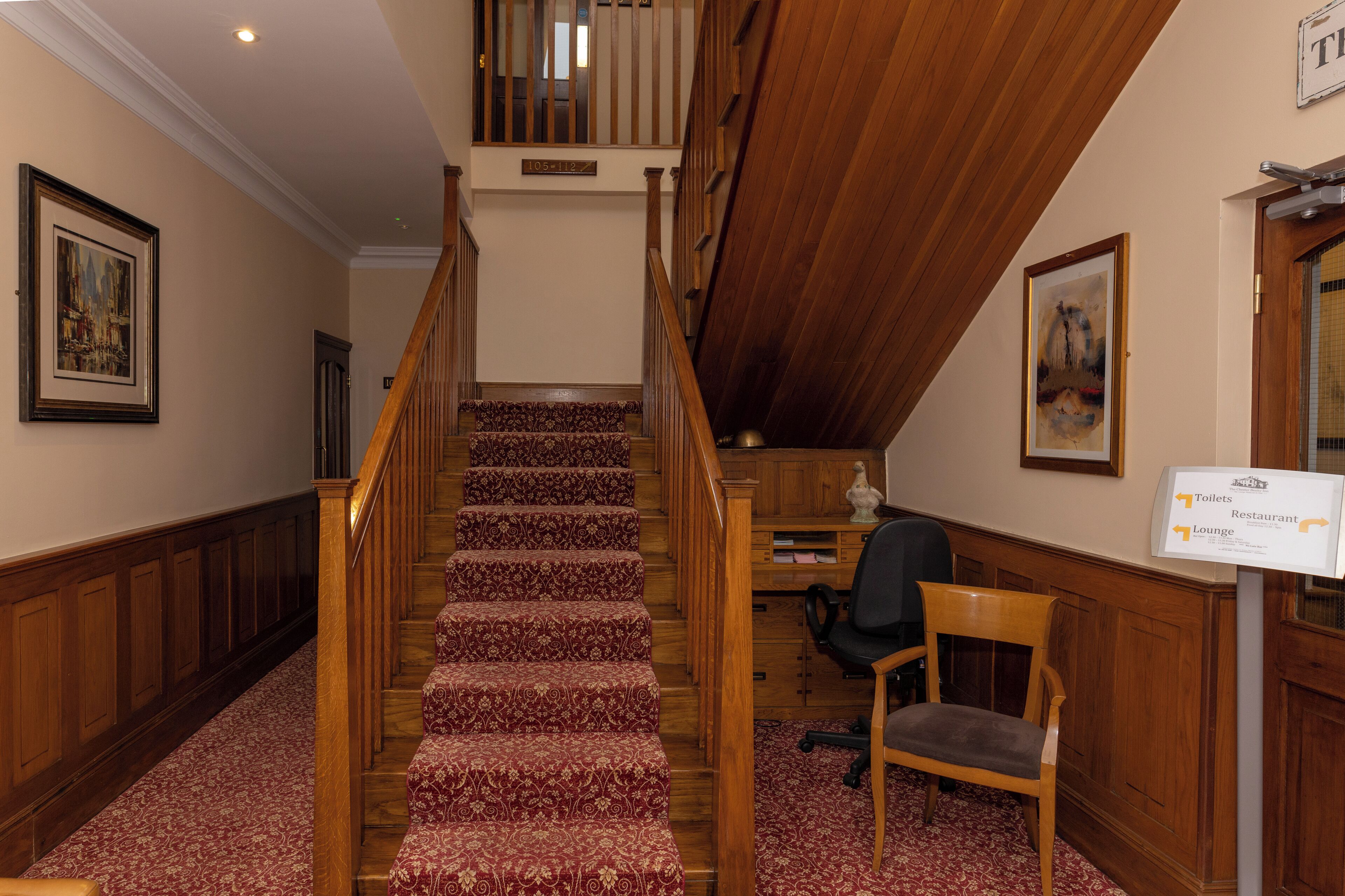 A staircase with a patterned carpet, wooden railings, and a sign indicating the location of the restaurant and lounge.