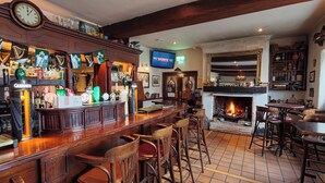 Een bar met houten barkrukken, een televisietoestel waarop Sky Sports te zien is, en een open haard.