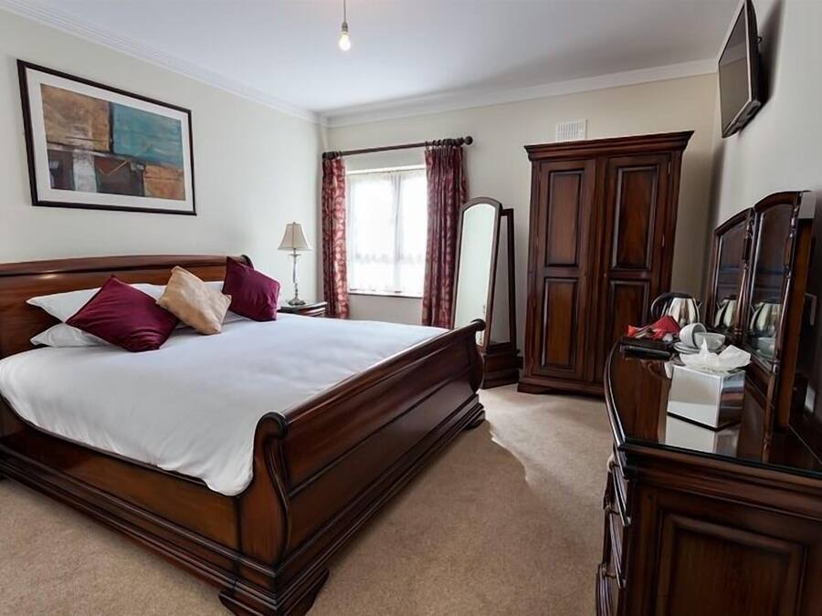 A hotel room with a large bed, wooden furniture, a mirror, and a painting on the wall.
